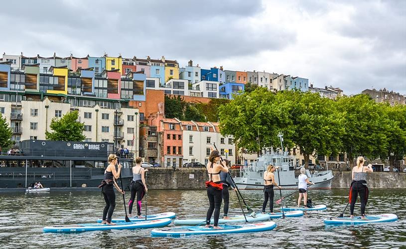 Paddleboarders float past colourful houses in Bristol